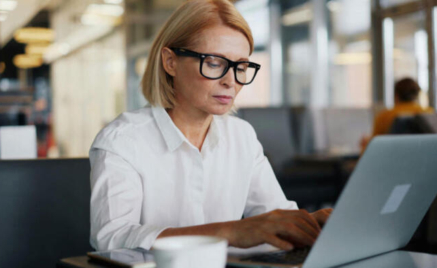 Person med vit skjorta och glasögon sitter vid datorn